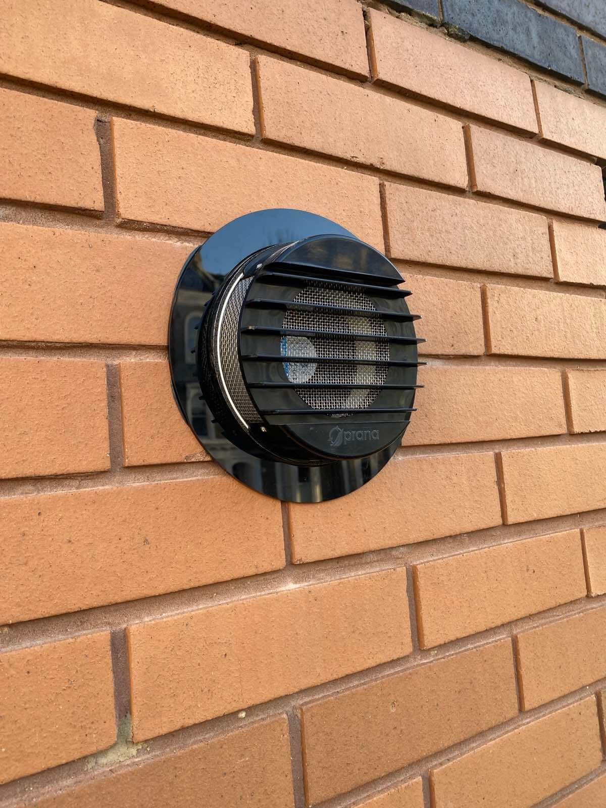 PRANA black plastic decorative ring installed on brick wall, enhancing ventilation system aesthetics.