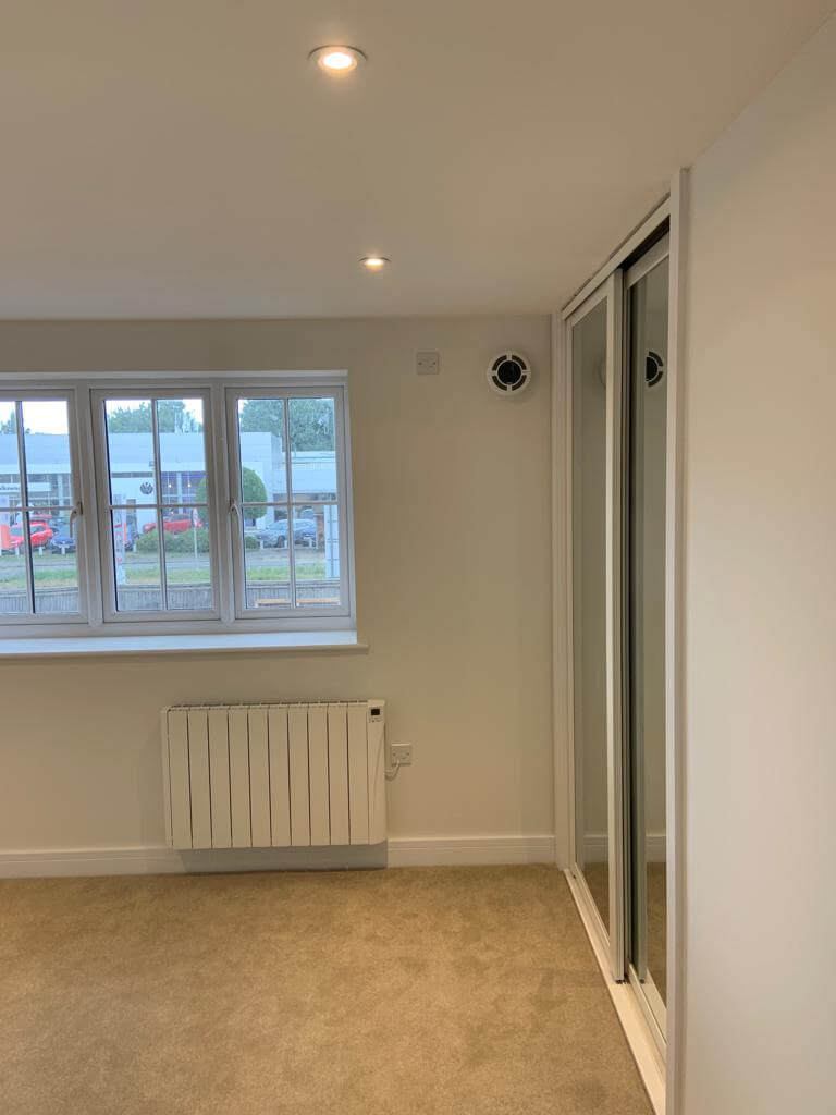 Interior view of a room showing windows, a heater, and a heat recovery ventilator for improved air quality.