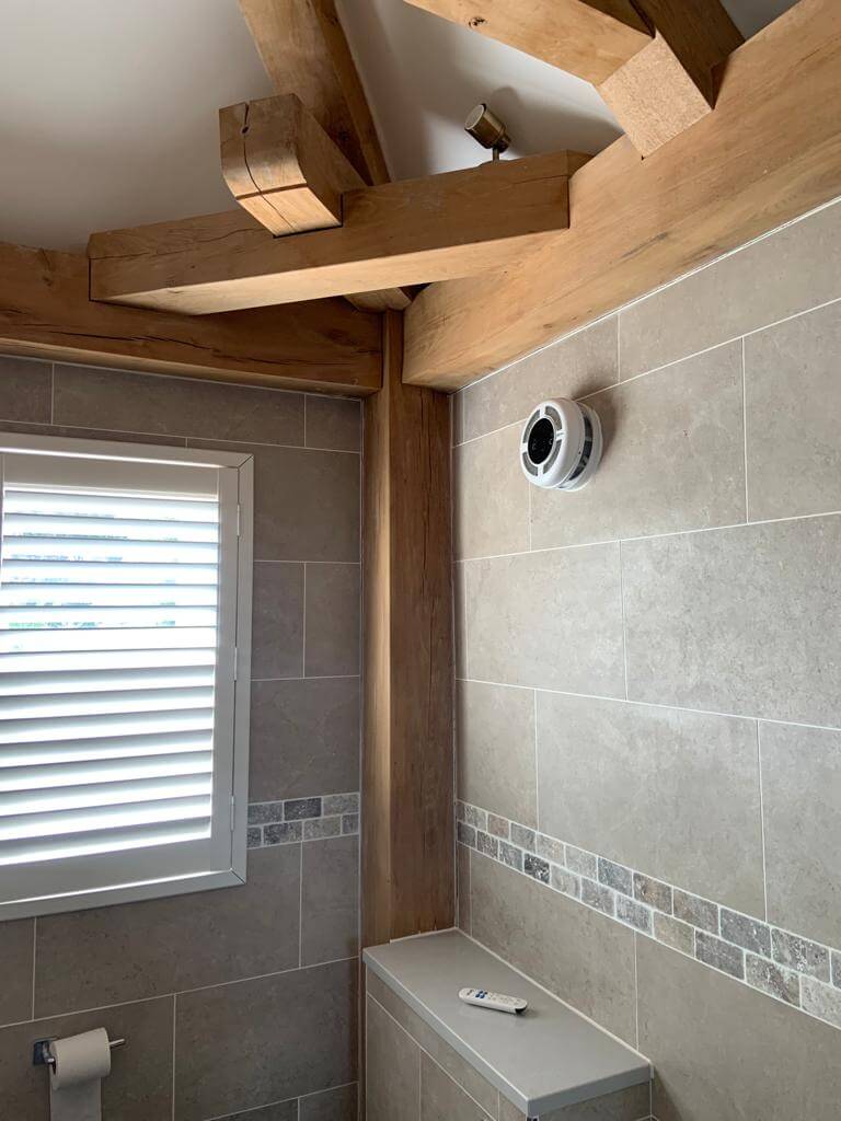 Heat recovery ventilation system installed in a modern bathroom with wooden beams and tiled walls.