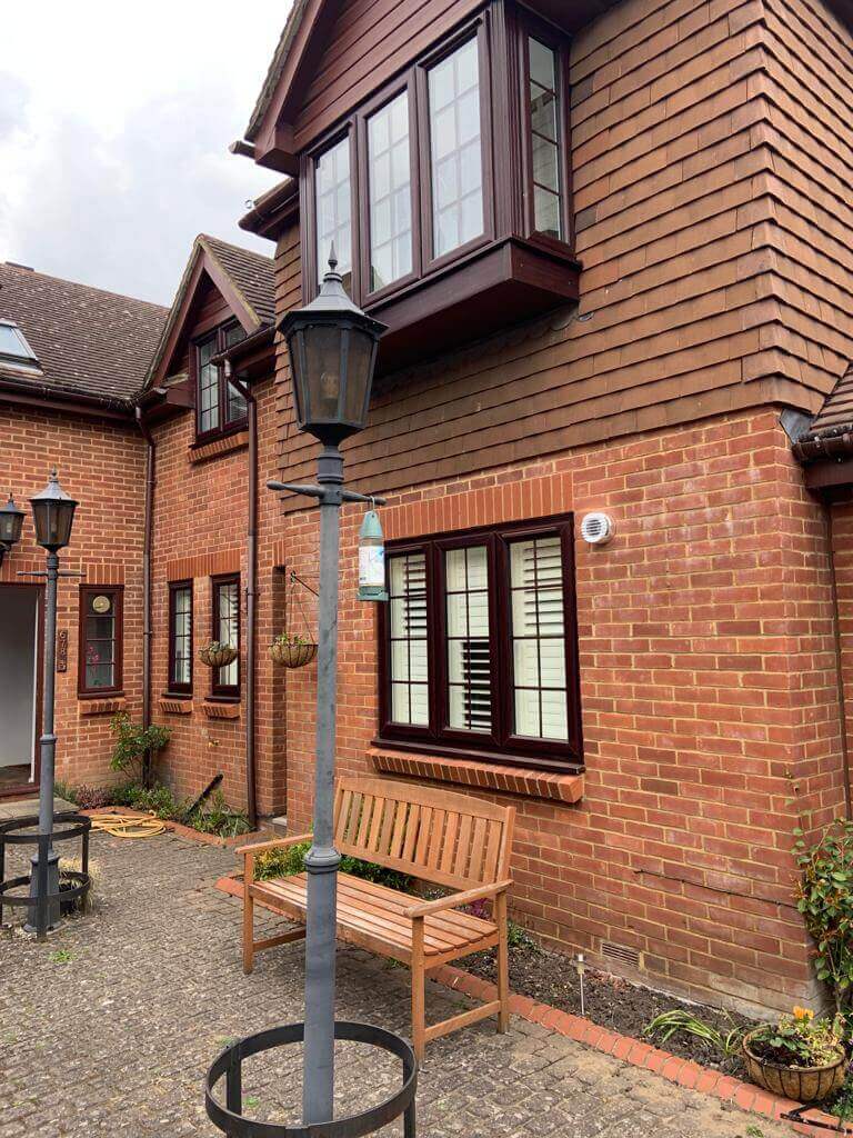 Exterior view of a charming brick house featuring windows, a bench, and decorative lamp posts.