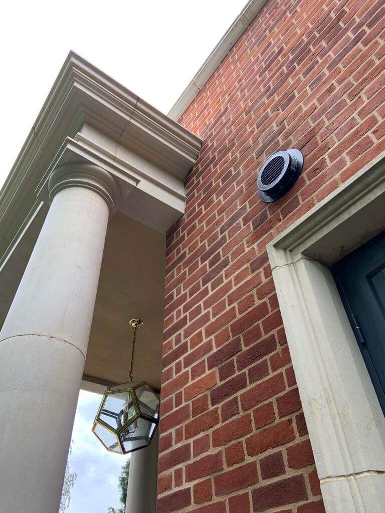 Exterior view of a brick building featuring a heat recovery ventilator mounted on the wall.