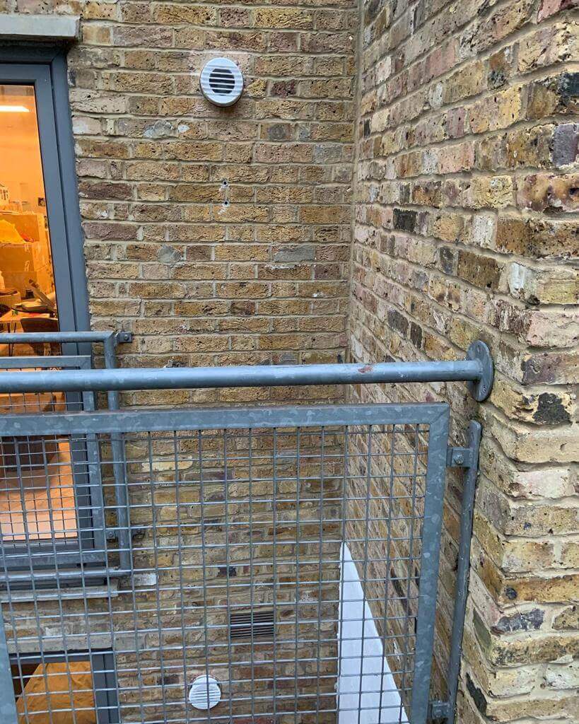 Exterior view of a building showing a heat recovery ventilation system installed on a brick wall.