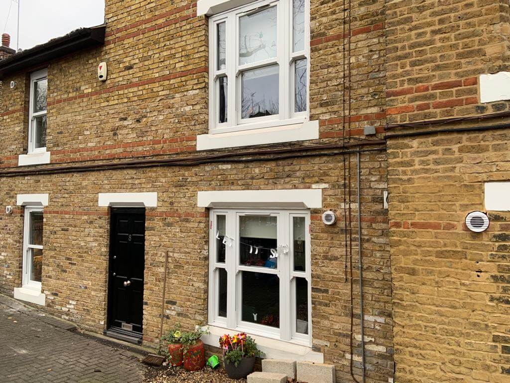 Exterior view of a brick house featuring windows, a black door, and decorative planters.