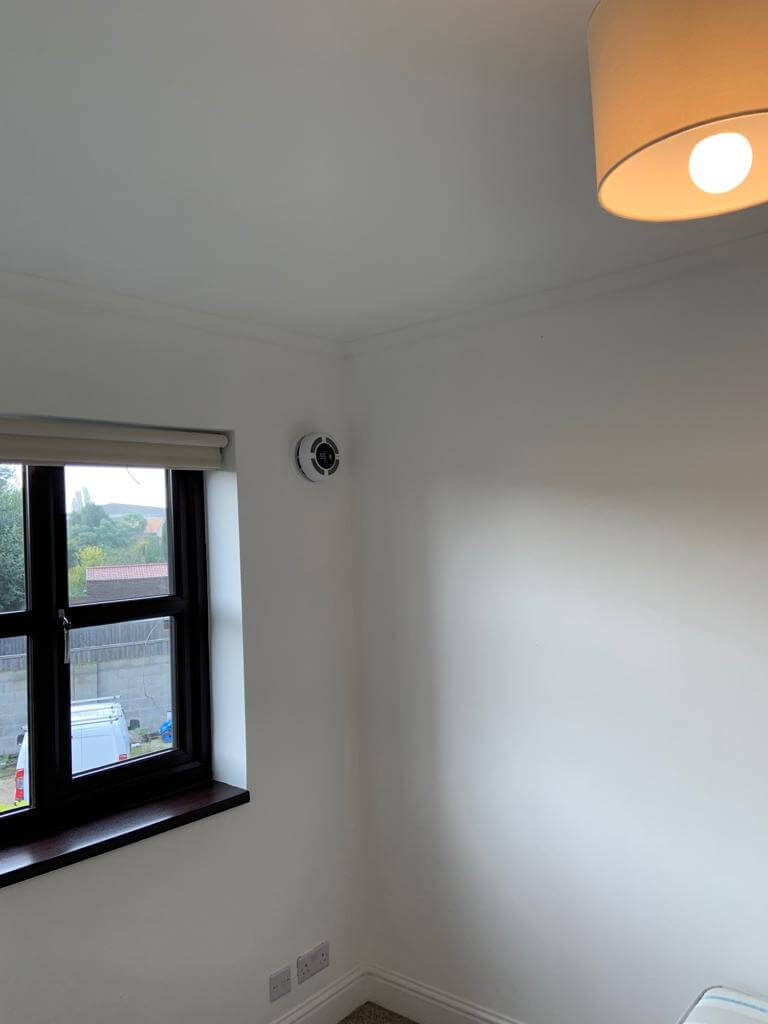 Heat recovery ventilation system installed on wall in a bright room with a window.