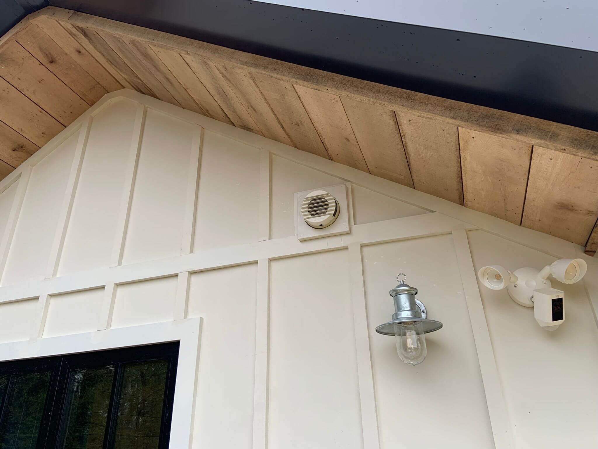 Exterior wall showcasing a heat recovery ventilator on a modern home with wood detailing and light fixtures.