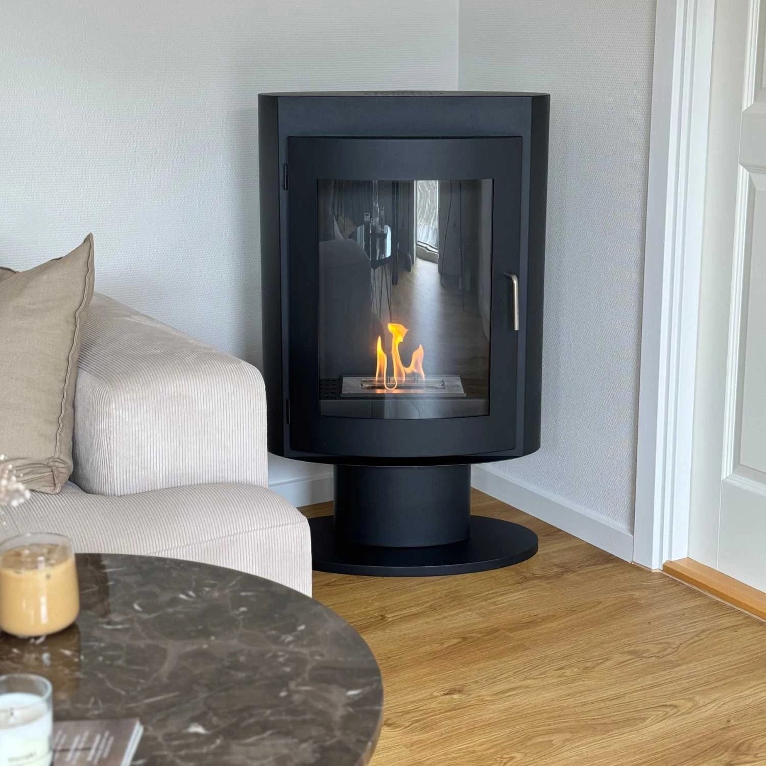 Trenton freestanding bioethanol stove on stand with flames, modern living room setting, black powder-coated steel design.