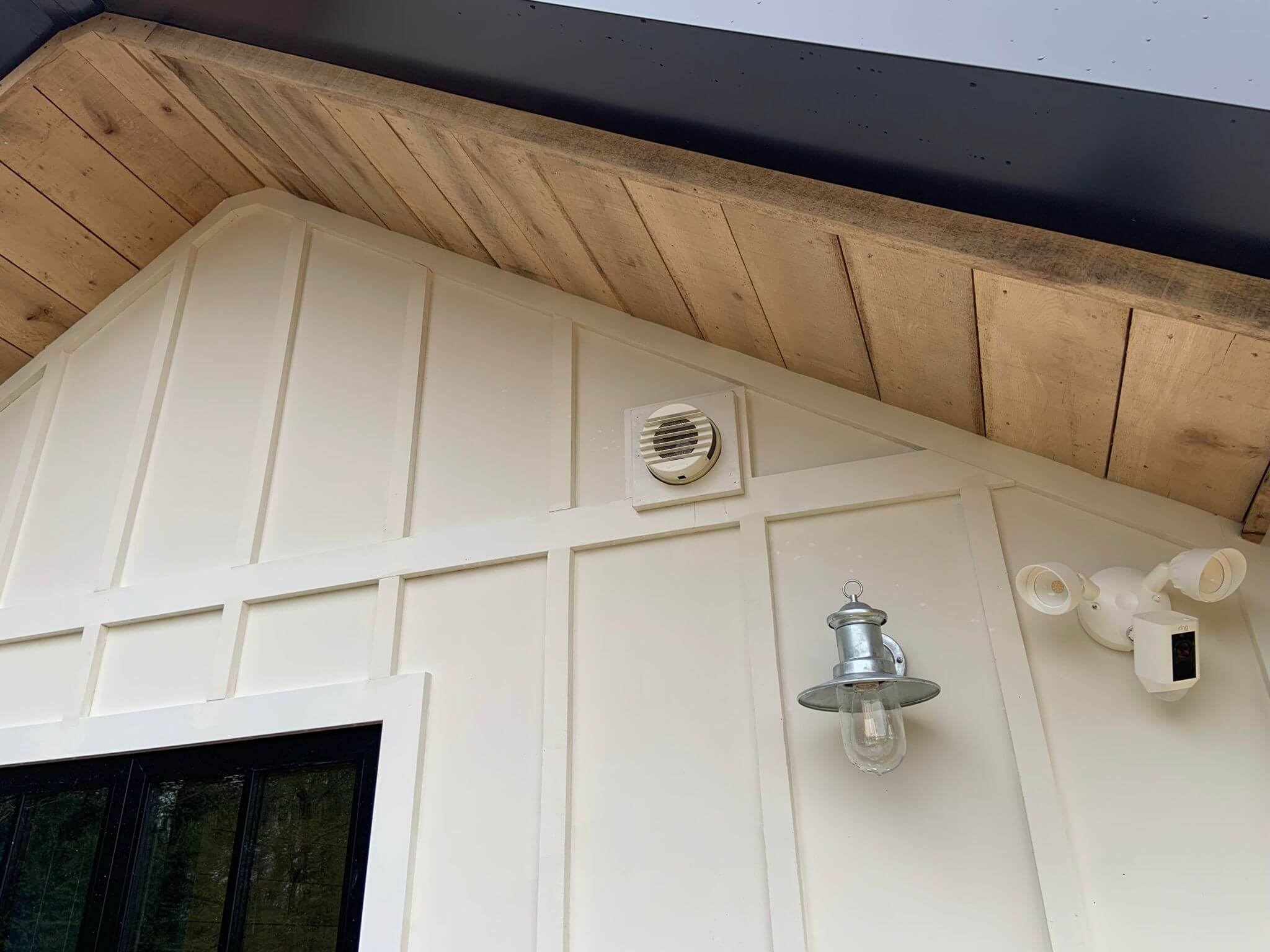 Exterior view of a house showing a heat recovery ventilator, accent lighting, and wooden ceiling details.