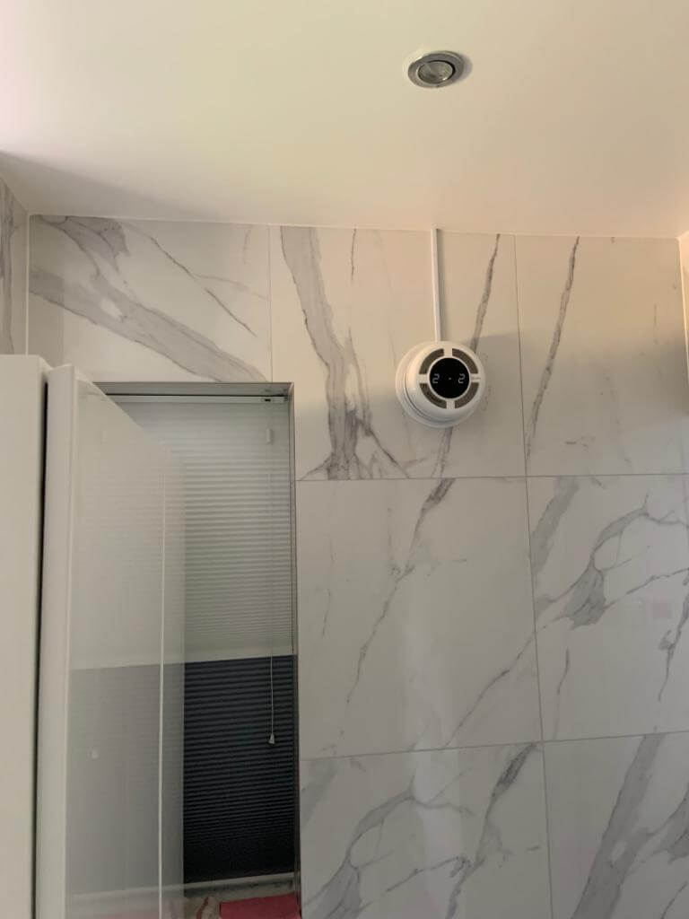 Wall-mounted heat recovery ventilator installed in a bathroom with marble tiles.