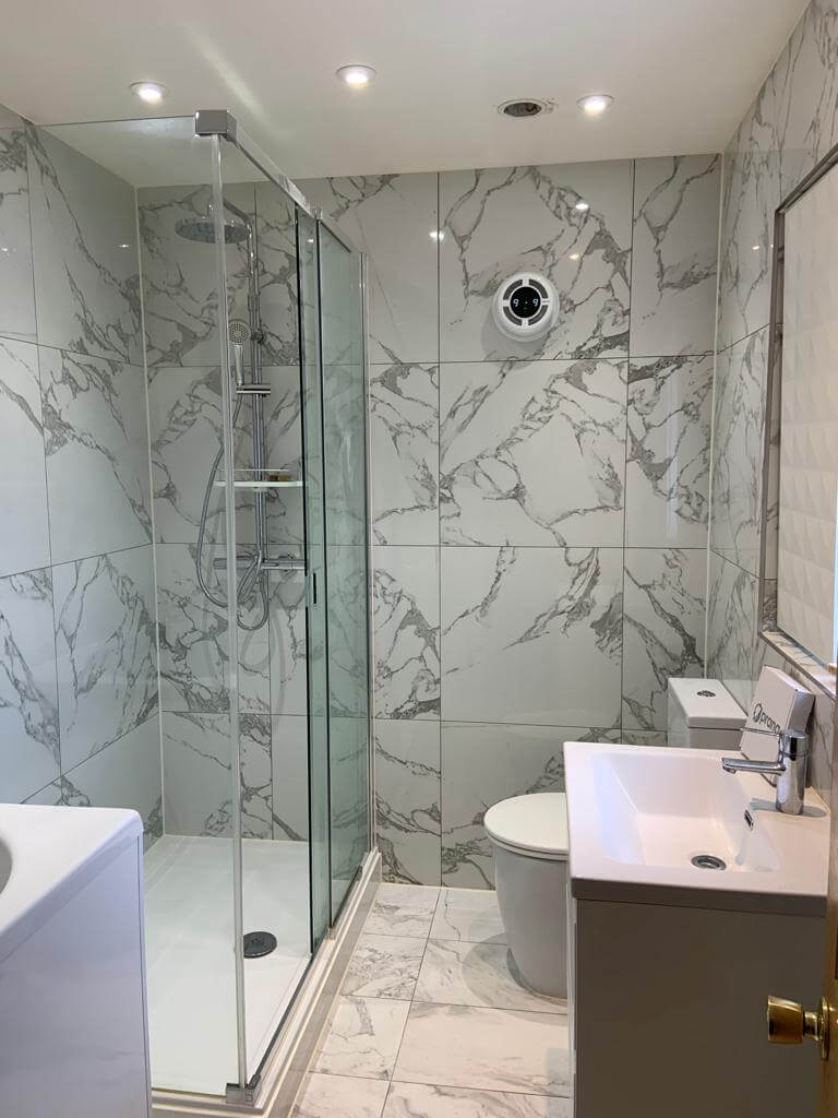 Modern bathroom with marble tiles, glass shower, and ventilation system for improved air quality.