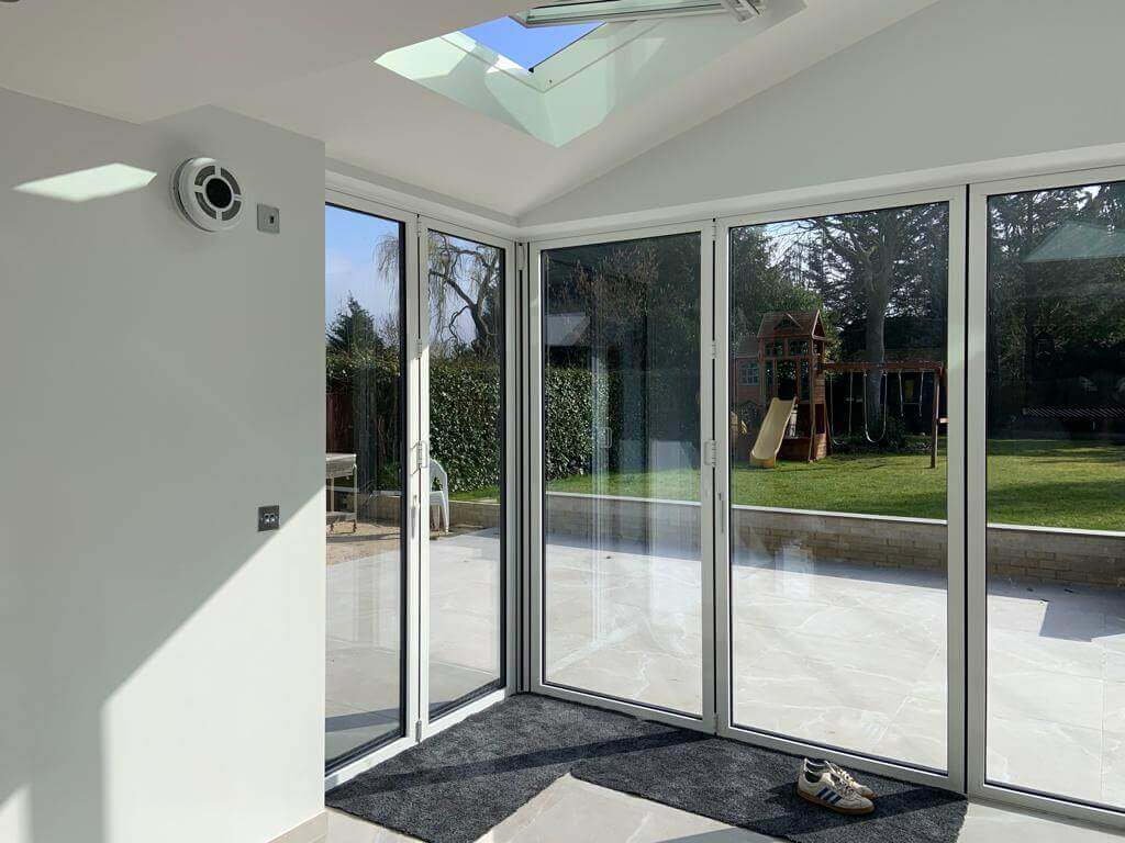 Interior view of a bright room featuring a heat recovery ventilator, large glass doors, and natural light.