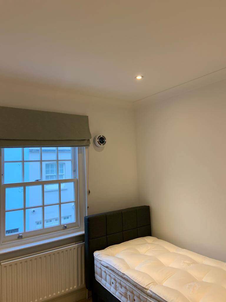 Room with single bed and a heat recovery ventilator installed near window.