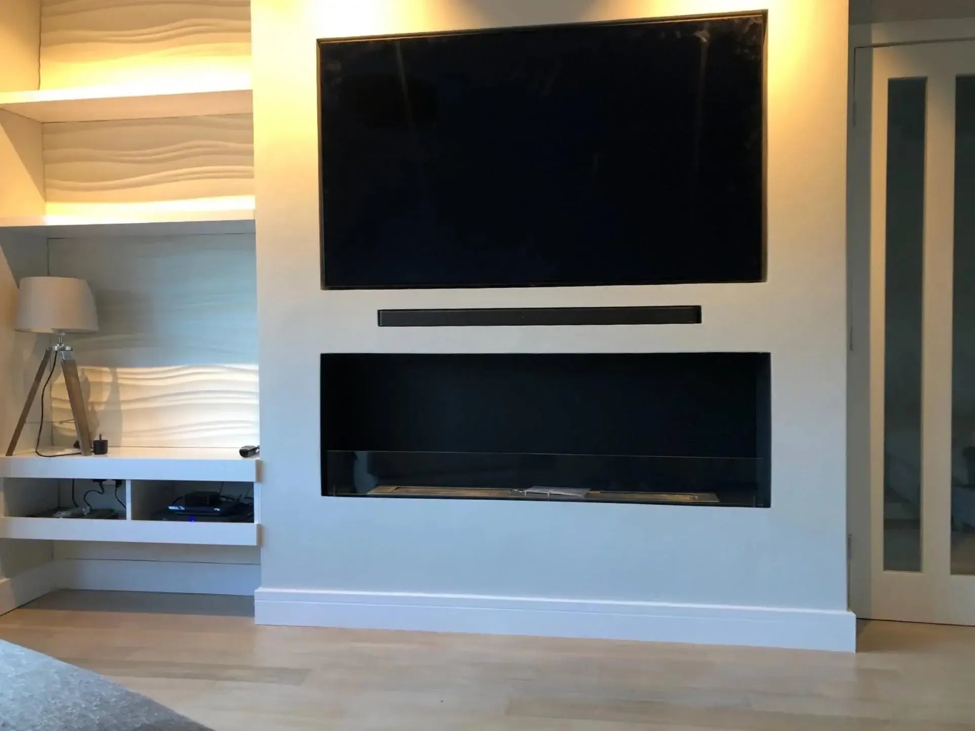 Modern living room with a built-in black bioethanol fireplace under a TV, featuring sleek design and media wall.