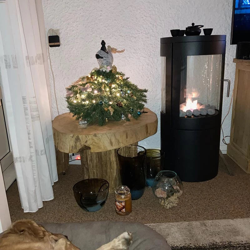 Decorative living room scene featuring a bioethanol stove, holiday tree, and various glass decor.