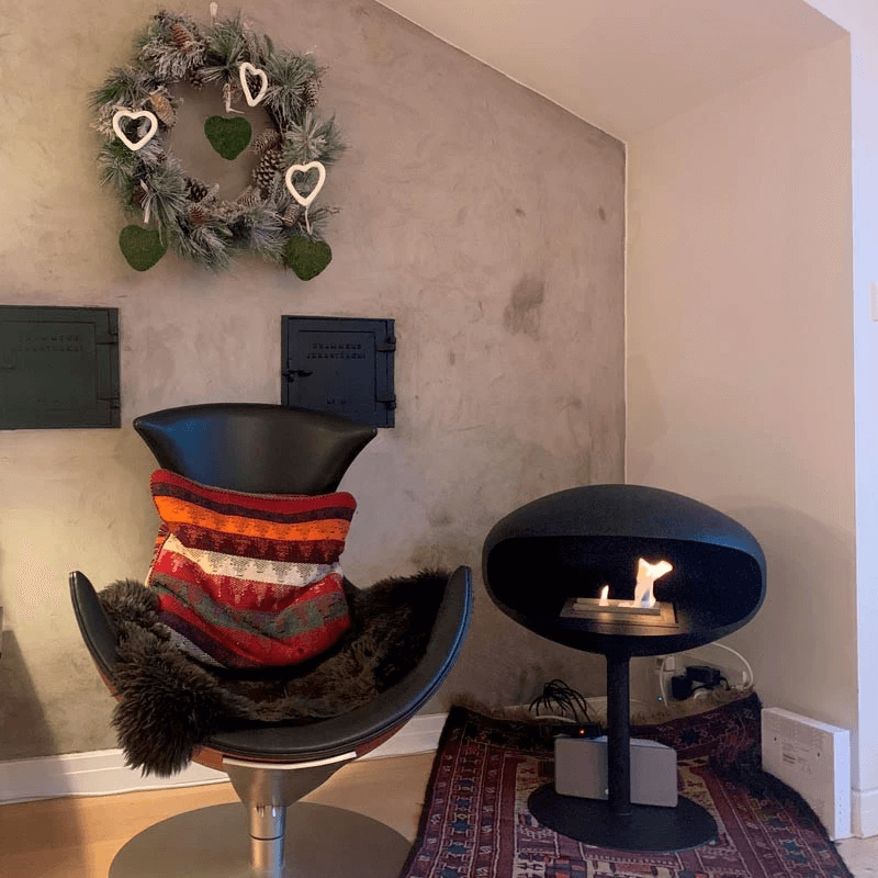 Modern black bioethanol fireplace next to a stylish chair with a colorful blanket, creating a cozy living space.