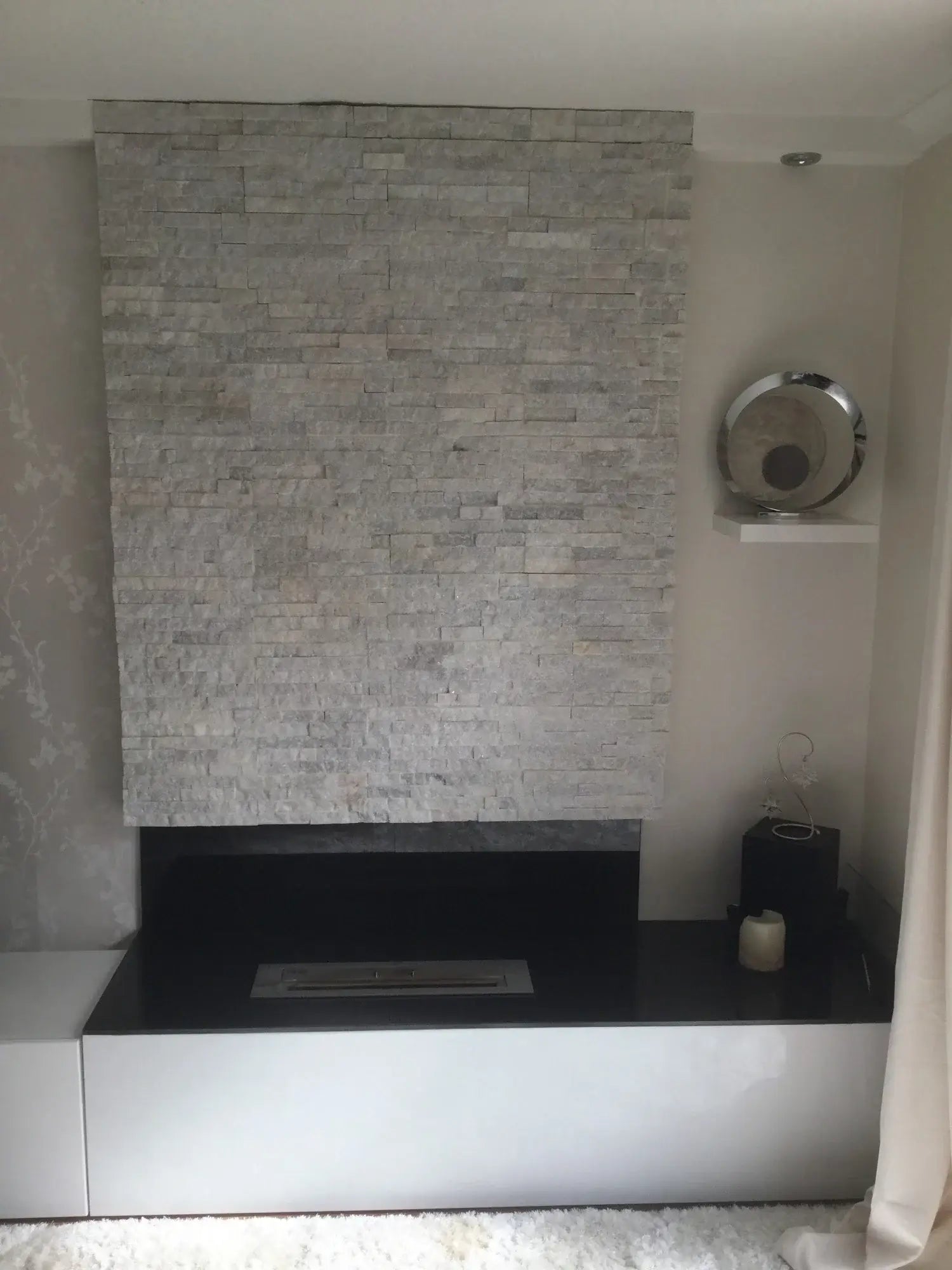 Modern bioethanol fireplace setup with stone wall and sleek black base, featuring a minimalist design.