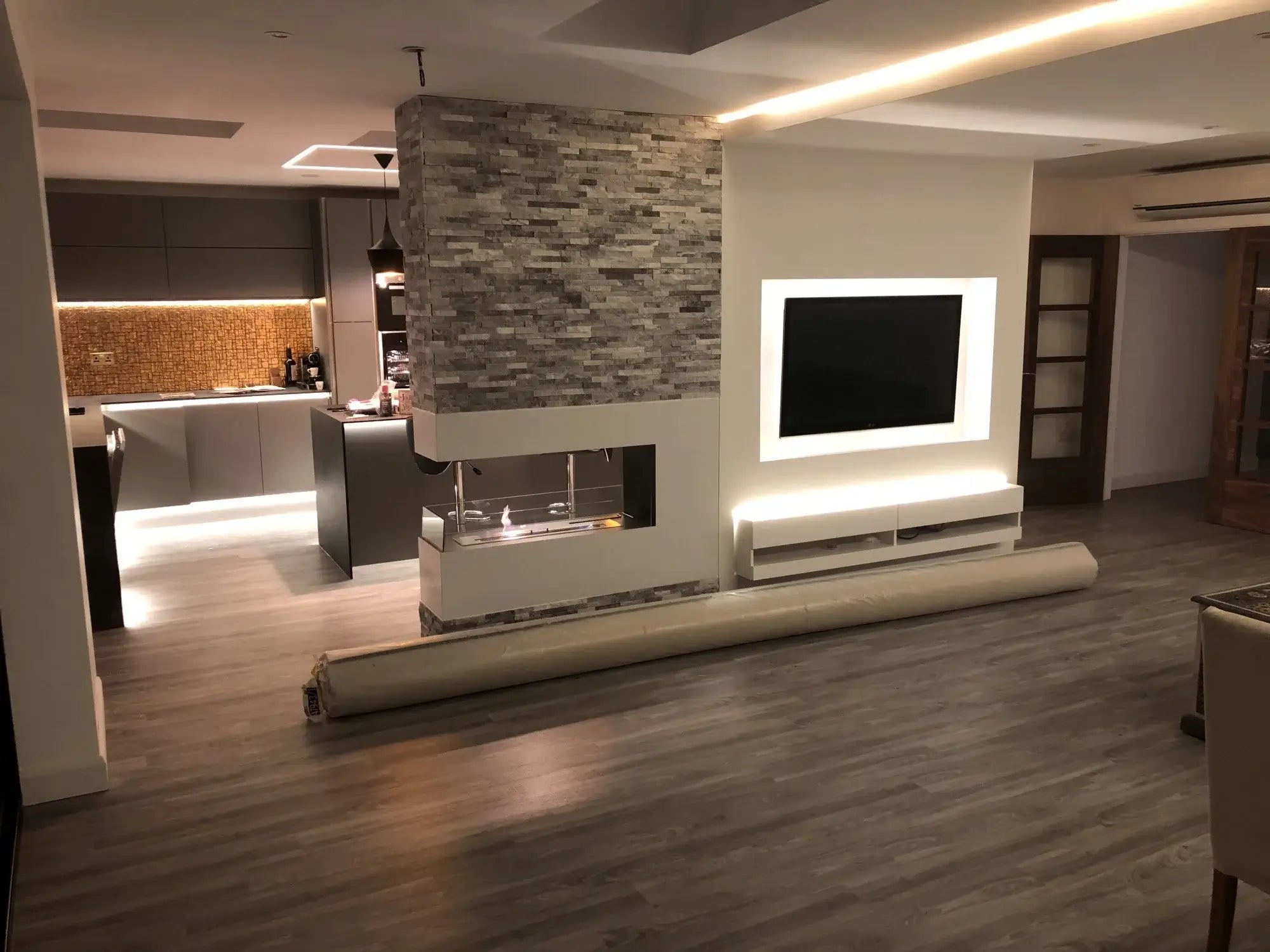Modern living room with a bioethanol fireplace and sleek kitchen design featuring a TV and contemporary lighting.