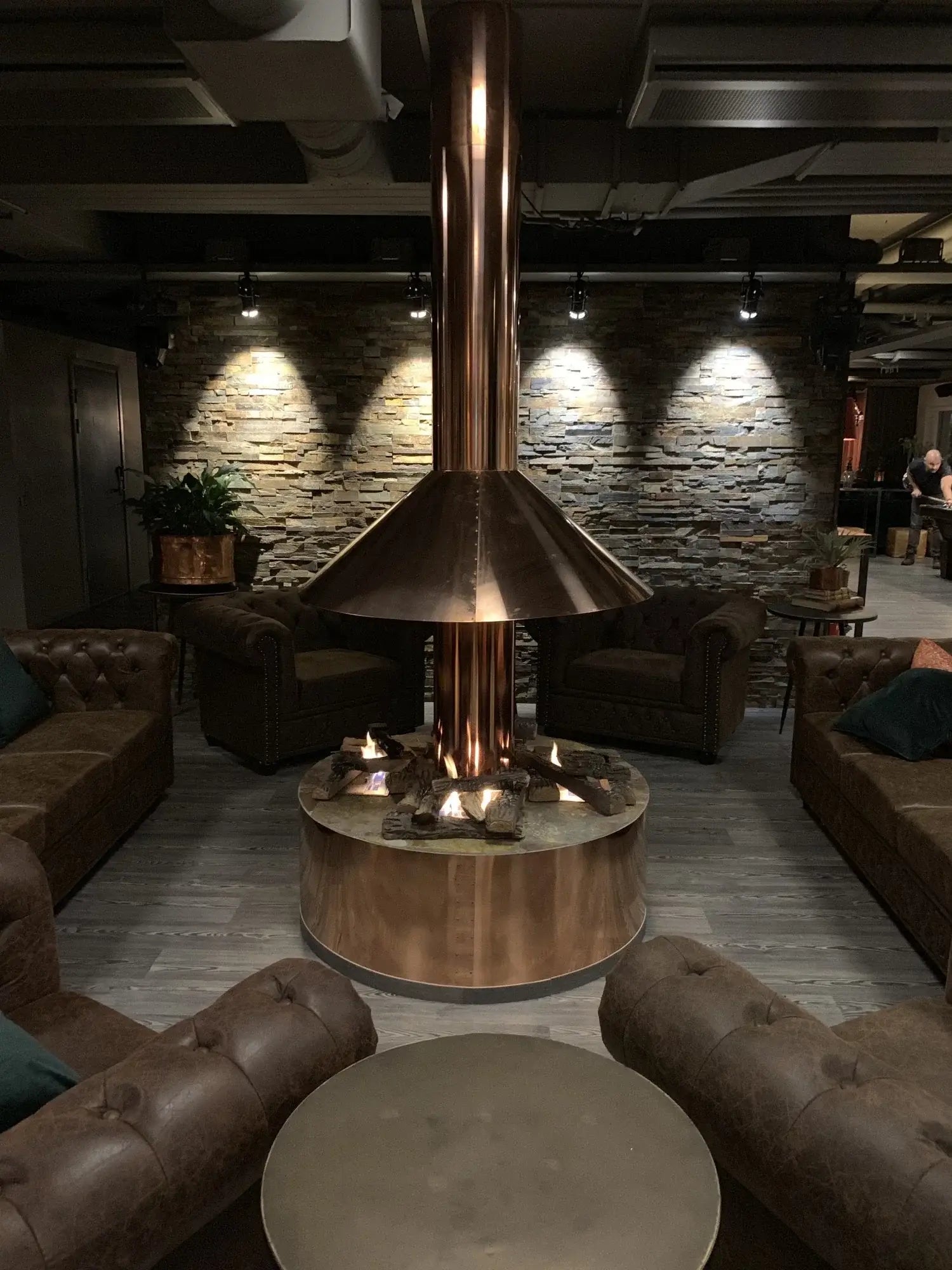 Modern lounge with copper fireplace surrounded by brown leather sofas, creating a cozy atmosphere.