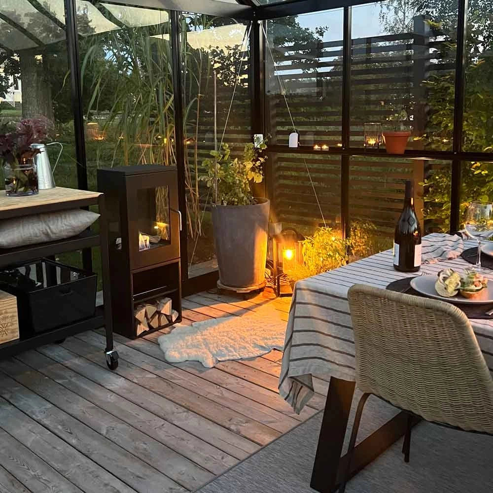 Cozy outdoor dining setup in a glass house with bioethanol fireplace, perfect for gatherings.