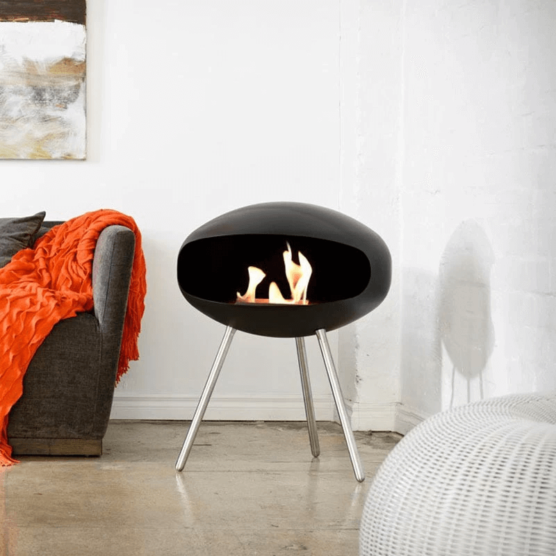 Cocoon Terra matte black bioethanol fireplace with steel legs in stylish living room setting.