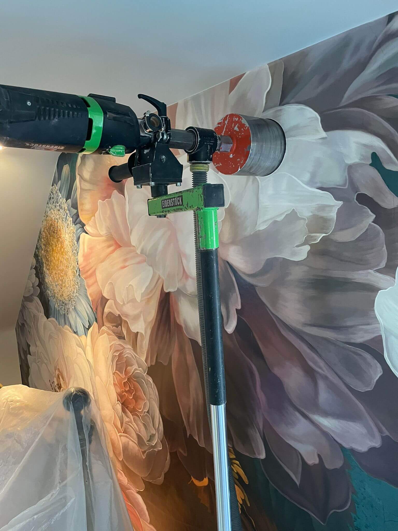 Drill tool mounted on wall, preparing for installation next to floral wallpaper decoration.