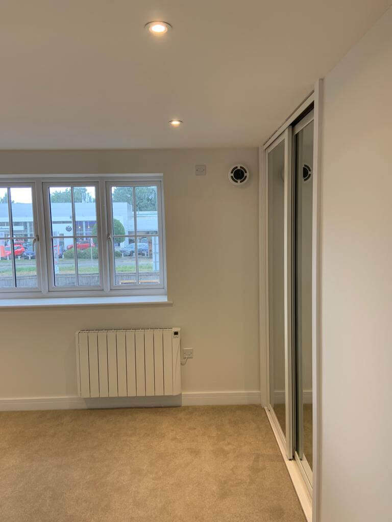 Modern apartment interior featuring a heat recovery ventilator, windows, and reflective wardrobes for ventilation.
