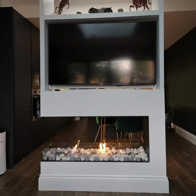 Modern bioethanol fireplace with glass, showcasing flames and elegant white stone decor beneath a wall-mounted TV.
