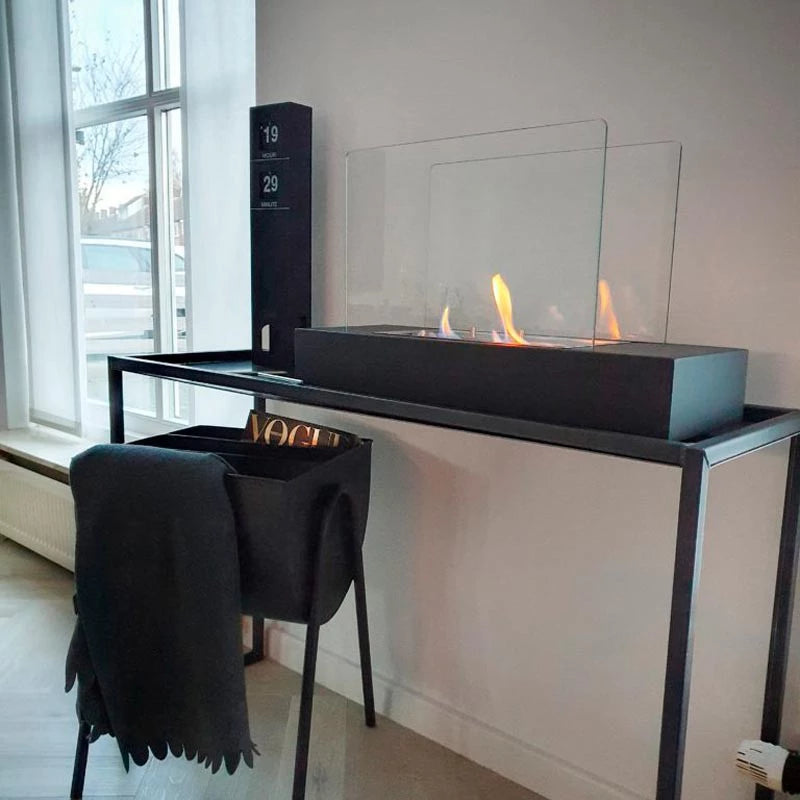 Freestanding black bioethanol fireplace with glass panels on a modern table in a stylish interior.