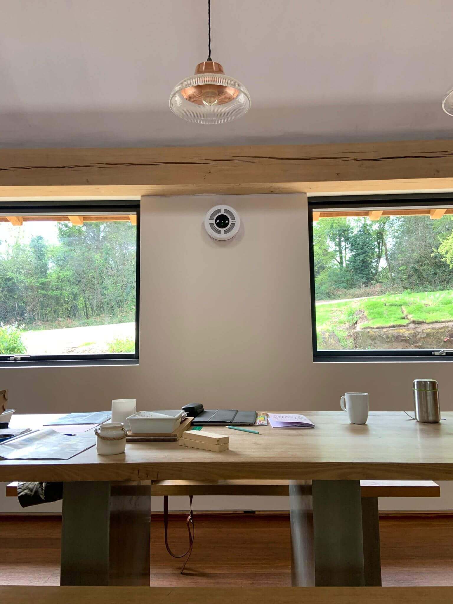 Interior view of a modern room featuring a heat recovery ventilator, large windows, and a wooden table.