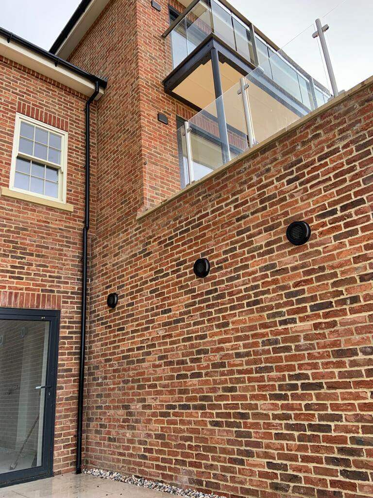 Exterior view of a brick building featuring a balcony and black ventilation grilles installed on the wall.