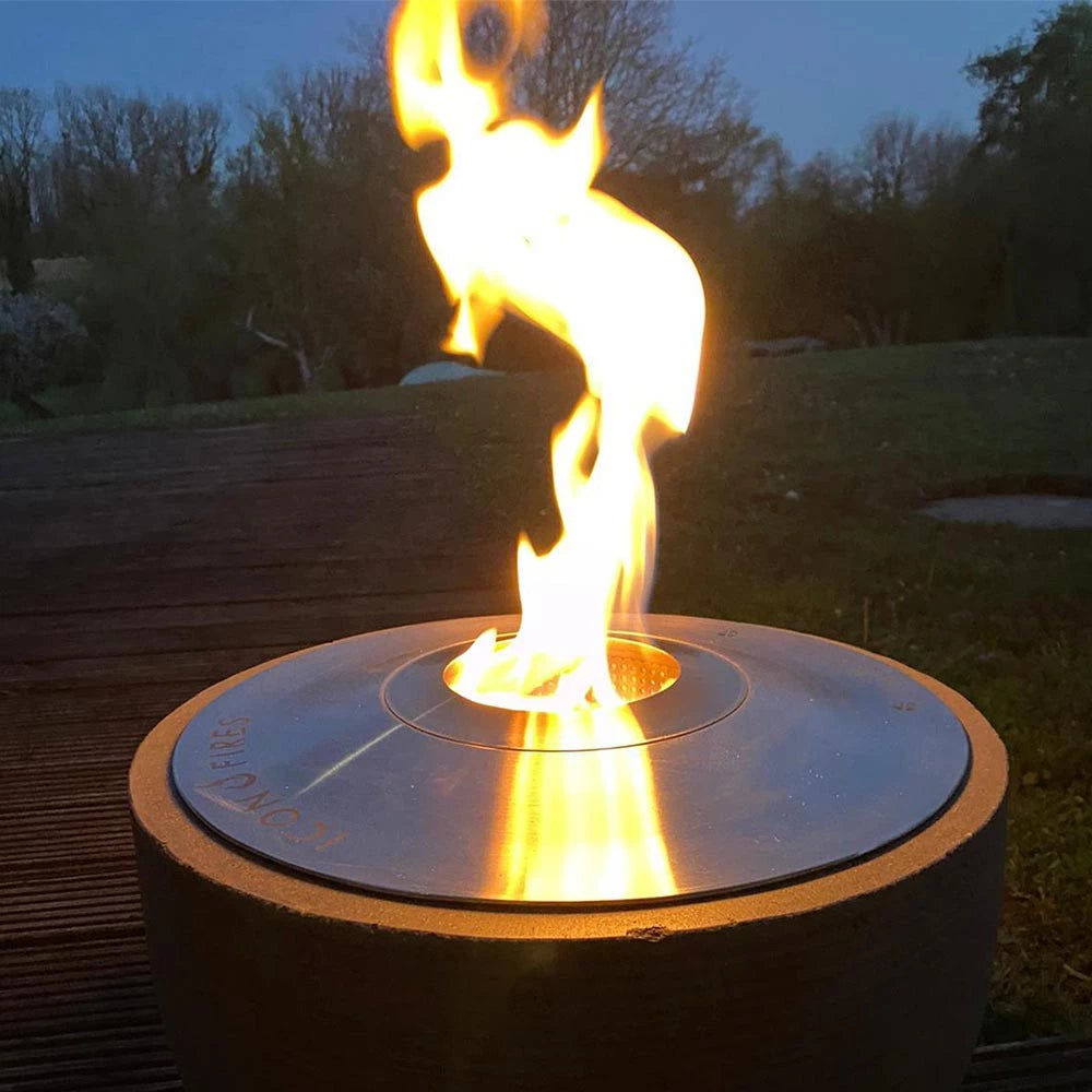 Icon Fires RD380 round bioethanol burner with vibrant flame, showcasing stainless steel design outdoors.