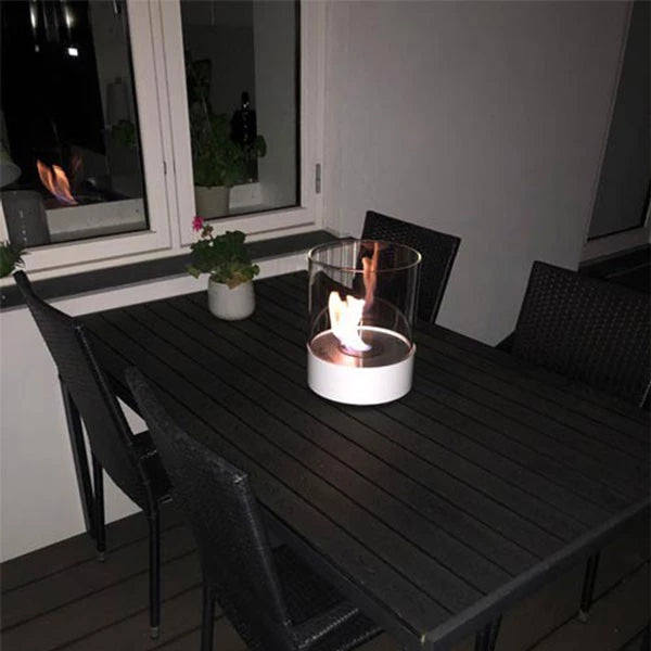 Southwark white tabletop bioethanol fireplace on a dark patio table, providing warmth and ambiance.
