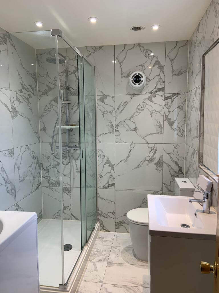 Modern bathroom with shower, marble walls, and ventilation system for effective air circulation.