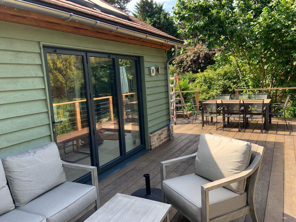 Cozy outdoor living space featuring seating and a dining area on a deck beside a green house.