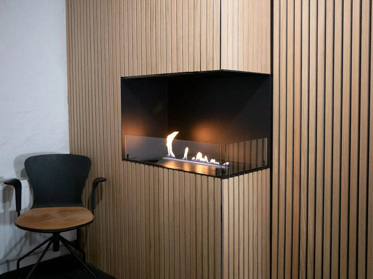 Elegant bioethanol fireplace insert built into a wooden wall, showcasing flames and modern design with a chair nearby.