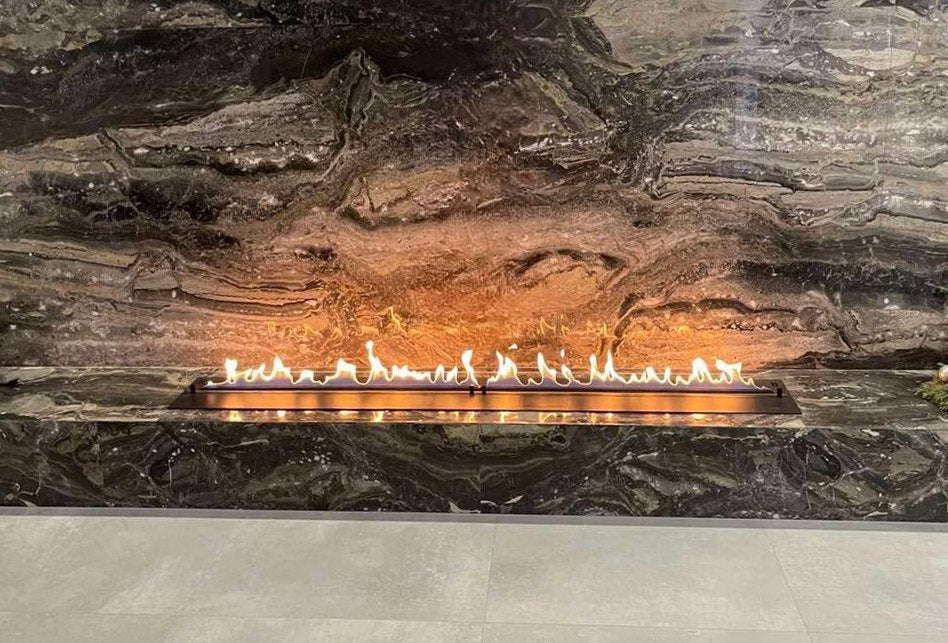 Sleek automatic bioethanol fireplace DALEX 3000 with flames against a textured stone wall.