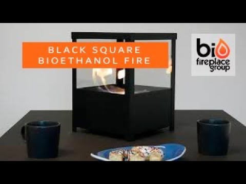 Black square bioethanol tabletop fireplace with flames, ideal for indoor or outdoor use, featuring a modern lantern design.