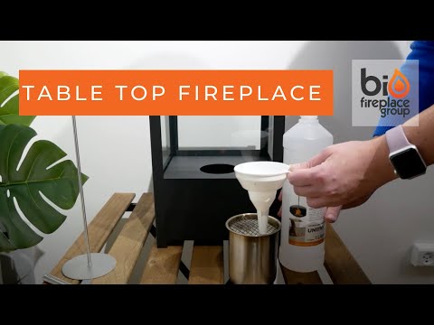 Person pouring bioethanol fuel into a black tabletop bio fireplace, showcasing its safe usage for indoor and outdoor settings.