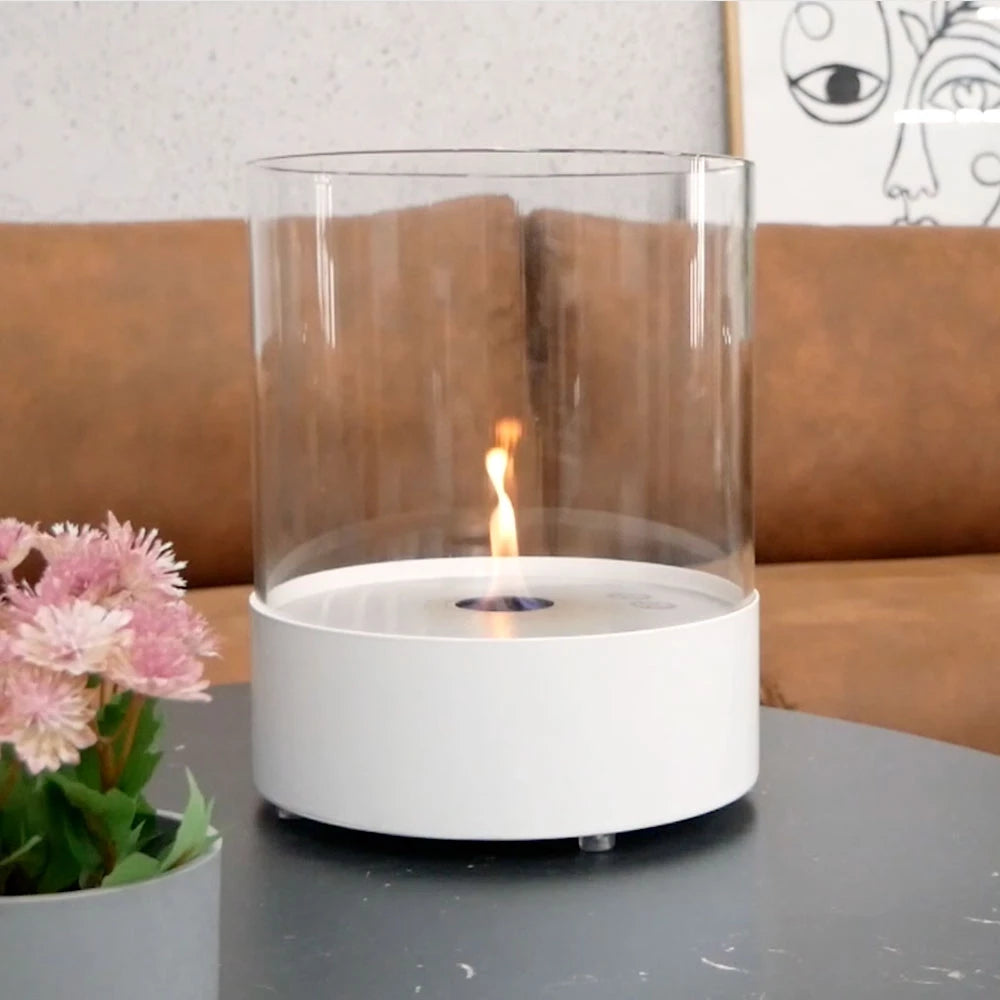 Southwark White round tabletop bioethanol fireplace with glass cylinder flame and flowers on a table.