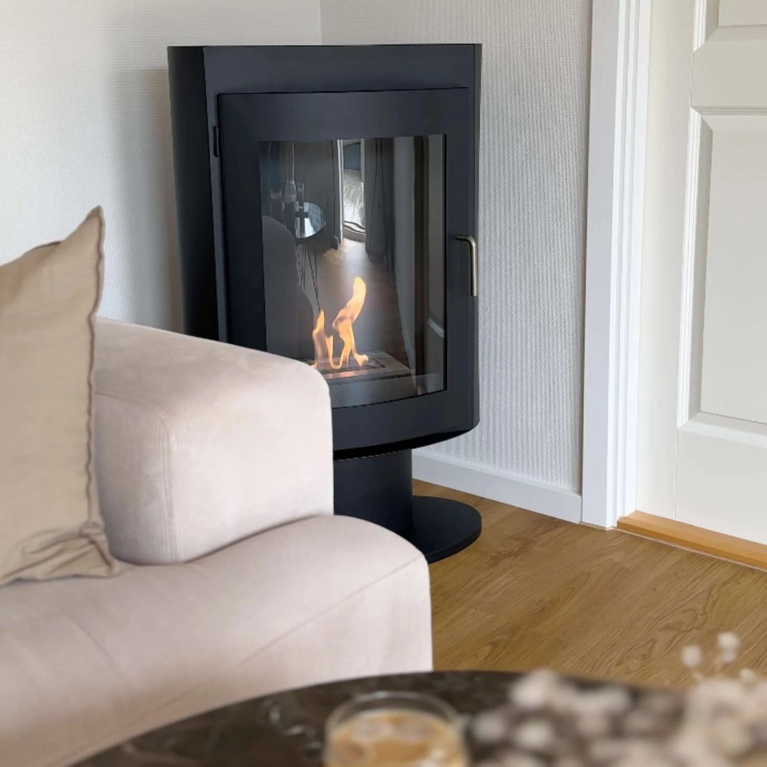 Trenton freestanding bioethanol stove in black steel, warm fire glow near a cozy sofa and wood floor.
