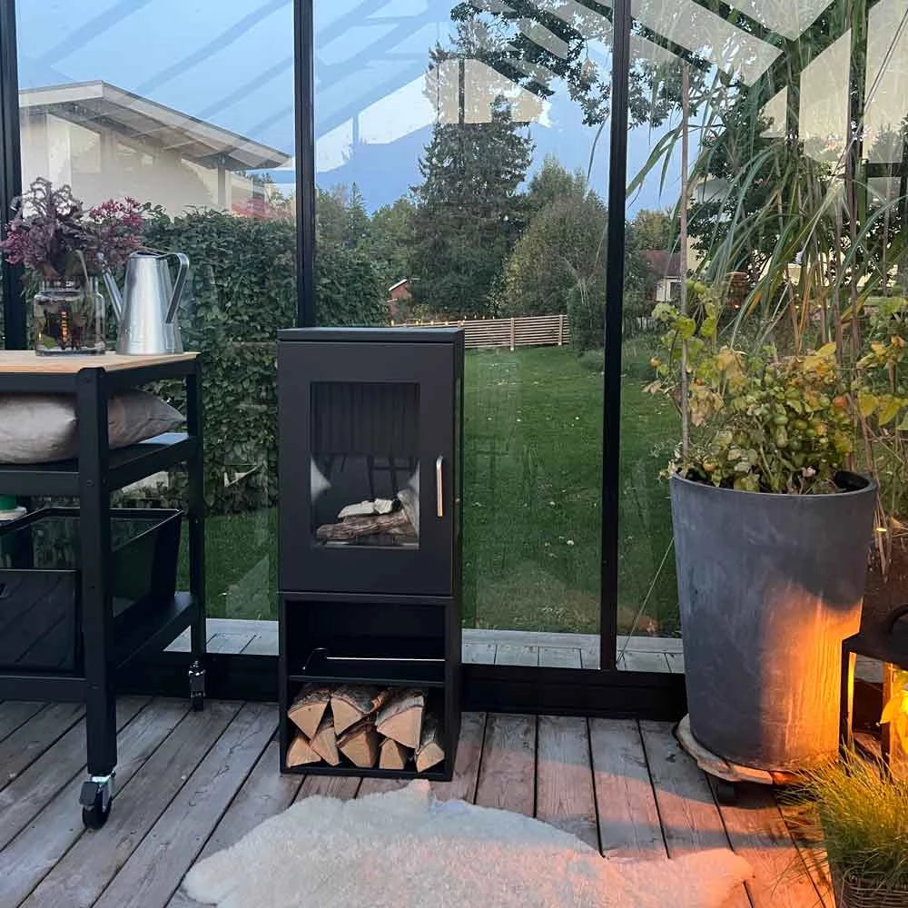 Cheyenne bioethanol stove fireplace in modern greenhouse setting with greenery and wooden deck.