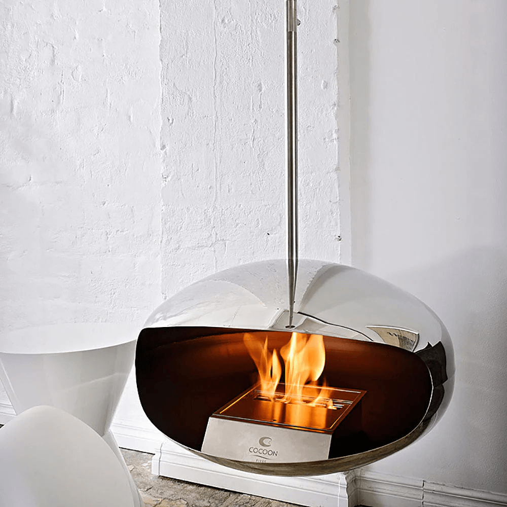 Cocoon Aeris polished steel bioethanol fireplace with flames, modern suspended design for stylish interiors.