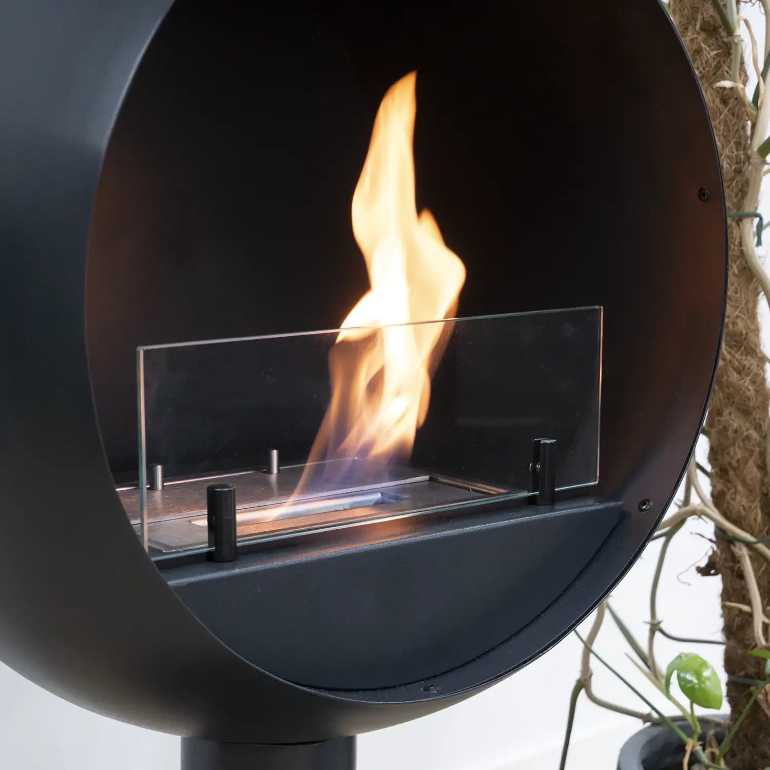 Close-up of Edmonton round freestanding bioethanol fireplace with flames visible through the glass panel.