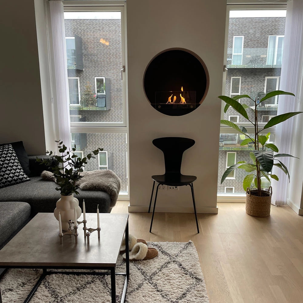 Contemporary round white wall mounted bioethanol fireplace in a stylish living room with plants and modern furniture.