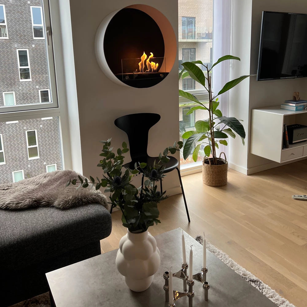 Contemporary round white wall-mounted bioethanol fireplace with flame, surrounded by modern living room decor.